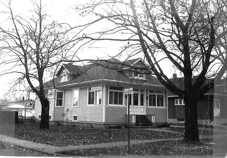 Black-and-white photo of a corner bungalow with an enclosed front porch, two leafless trees in the yard, and a "Morgan St" street sign.