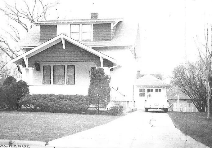 Front view of a two-story Craftsman-style house with a driveway leading to a detached garage and a parked car.