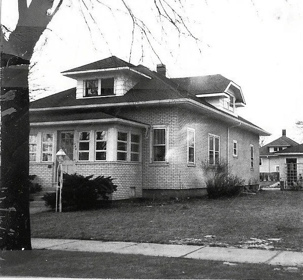 Black-and-white photo of a two-story early 20th-century bungalow with a hipped roof, enclosed front porch, and grassy front yard. (Copy)