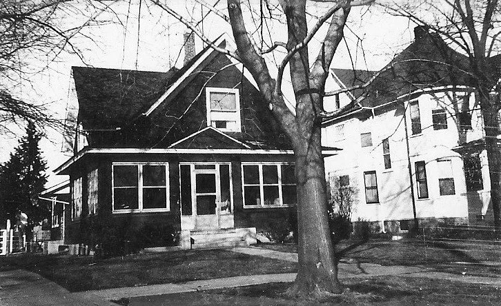 Black-and-white photo of two adjacent early-20th-century houses with a large leafless tree in the front yard and an enclosed front porch on the nearer house.