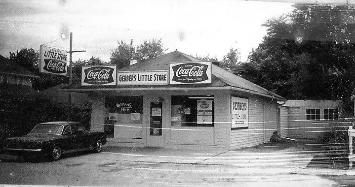 Black-and-white photo of Gerber’s Little Store storefront with Coca-Cola signs and a vintage car parked in front.
