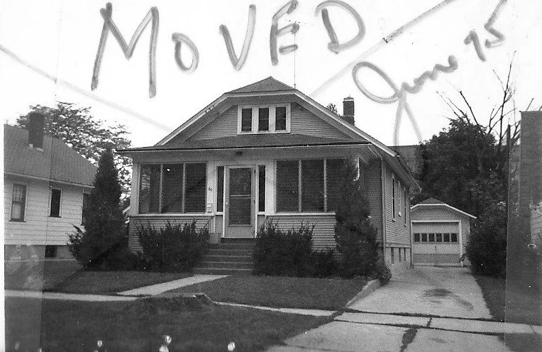 Black-and-white photo of a single-story bungalow with a screened front porch, driveway leading to a detached garage