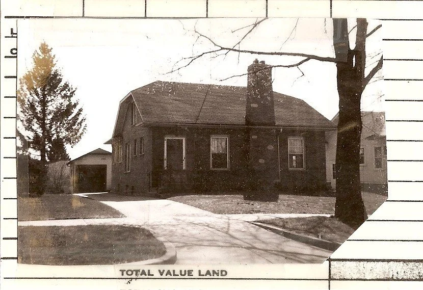 Black-and-white photo of a one-story brick house with central chimney, driveway to a detached garage; caption reads "TOTAL VALUE LAND".