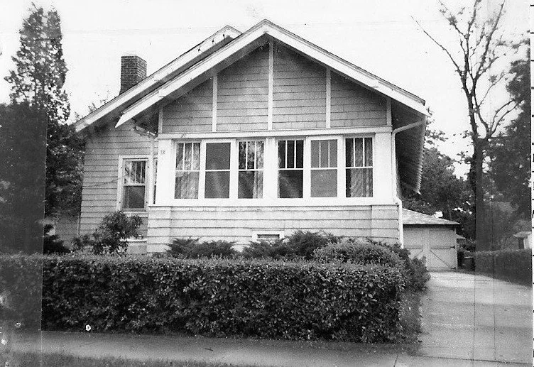 Bungalow-style house with an enclosed front porch, trimmed hedge, driveway, and detached garage.