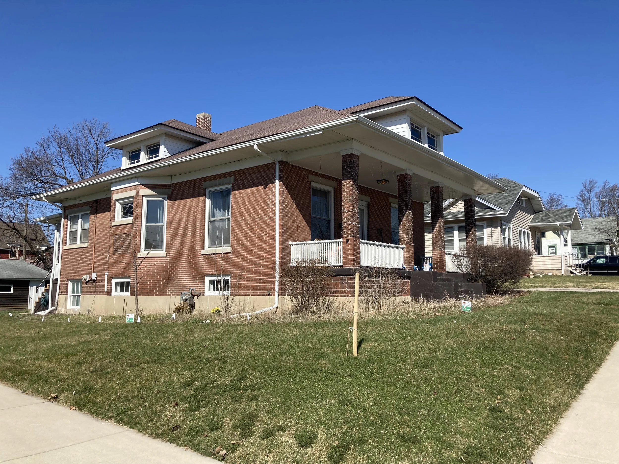 Brick two-story house with front porch, dormer window, chimney, and clear blue sky.