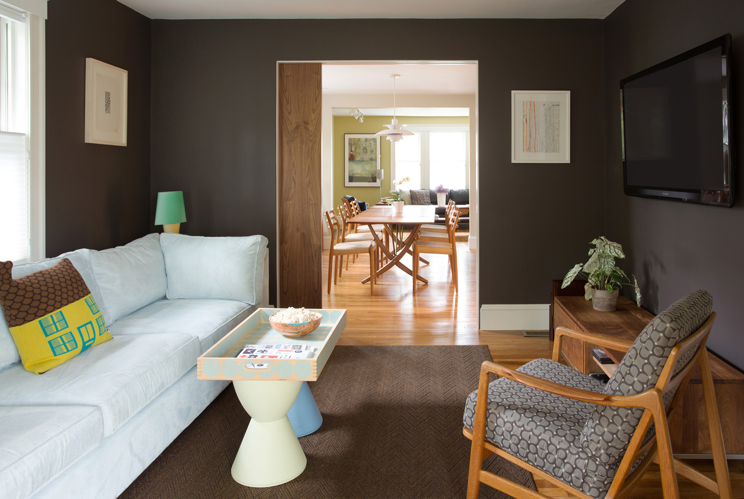 A modern walnut pocket door divides the dining room from the T.V. room, where walls are painted dark to disguise the wall-hung television.