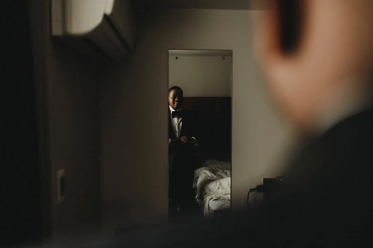 african groom looking in mirror before wedding ceremony at hylands house