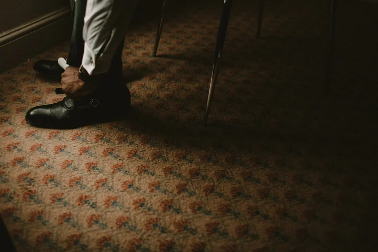 groom ties his laces whilst getting ready for froyle park wedding