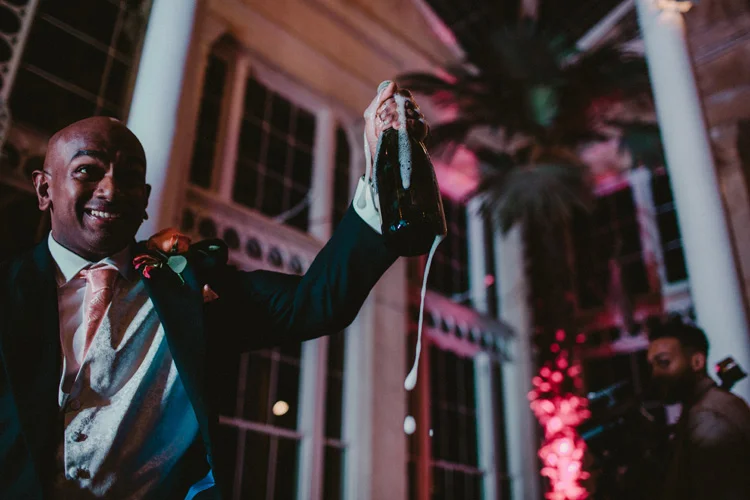 groom opens champagne during syon park wedding reception