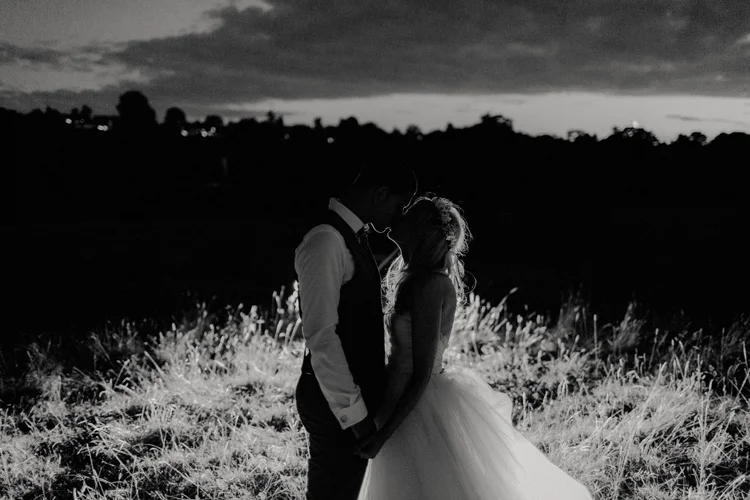 boho bride and groom share kiss in front of car headlights in chesham wedding