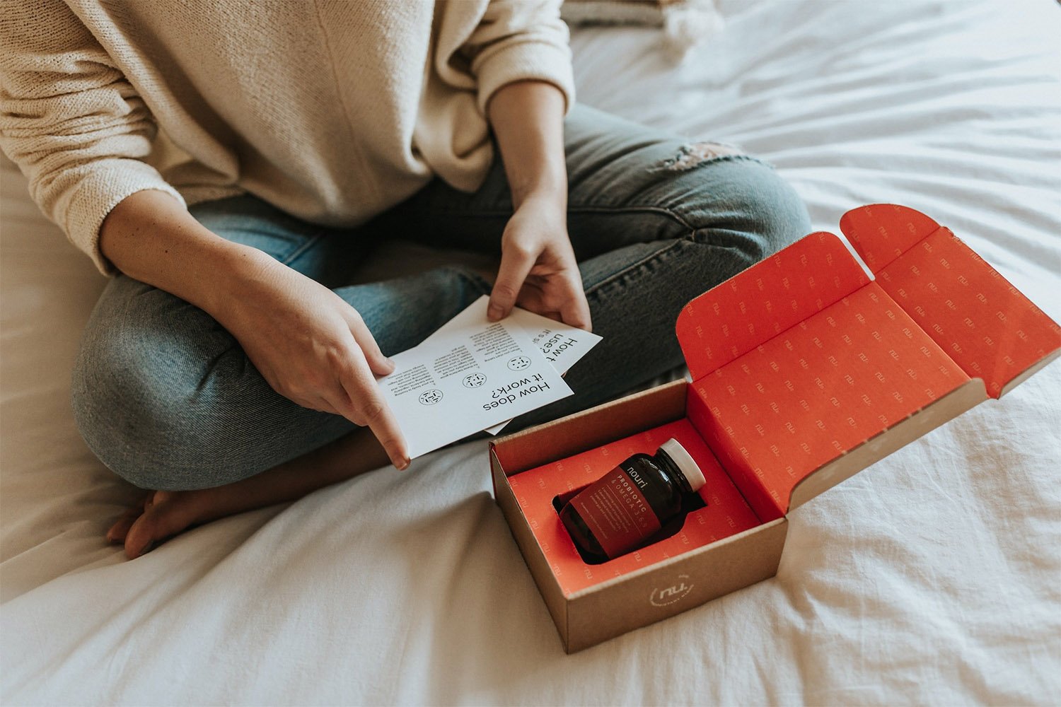 A person sitting on a bed opening a box with a bottle inside