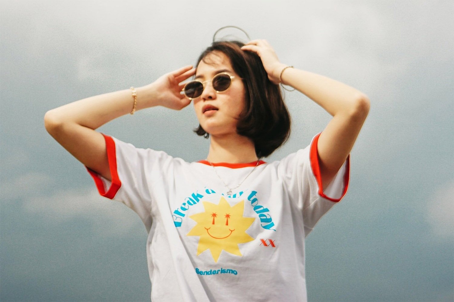 A young woman wearing sunglasses and a white shirt with a sun on it.