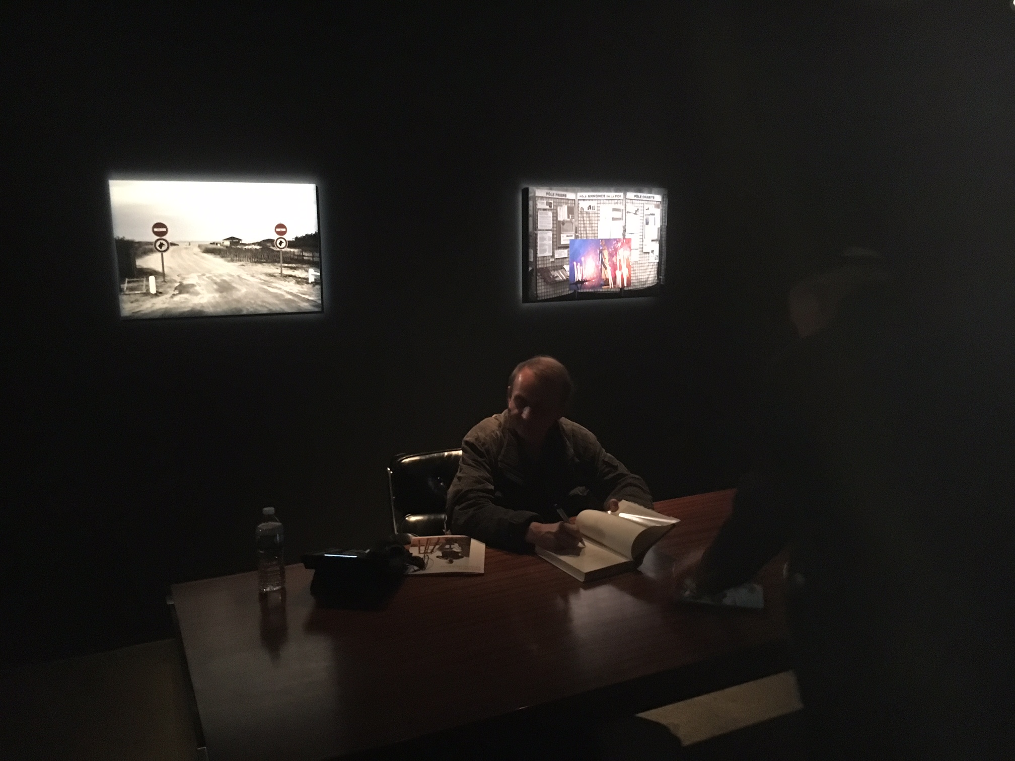 Novelist, poet, and artist Michel Houellebecq signing copies in the dark at the opening of his show "Michel Houellebecq: French Bashing" on Friday in New York. Photo Credit: Joel Whitney