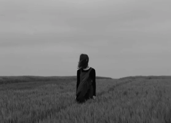 black and white of a girl in a field of high grass with hair in face