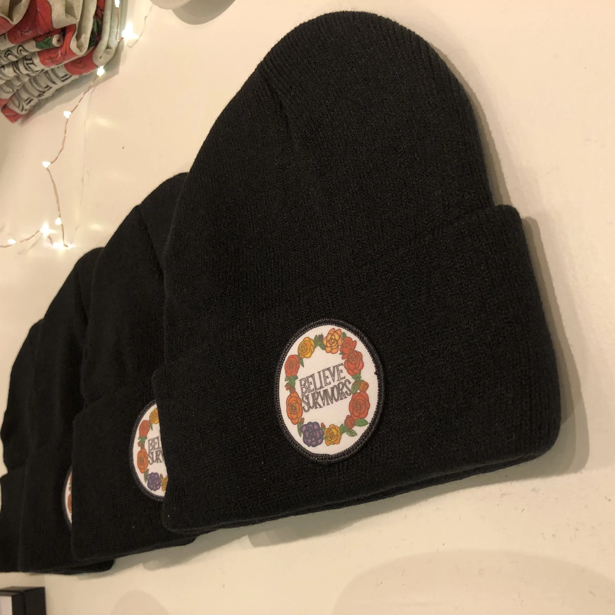 black unisex beanie with embroidered patch ring of flowers "believe survivors" text - dfrntpigeon
