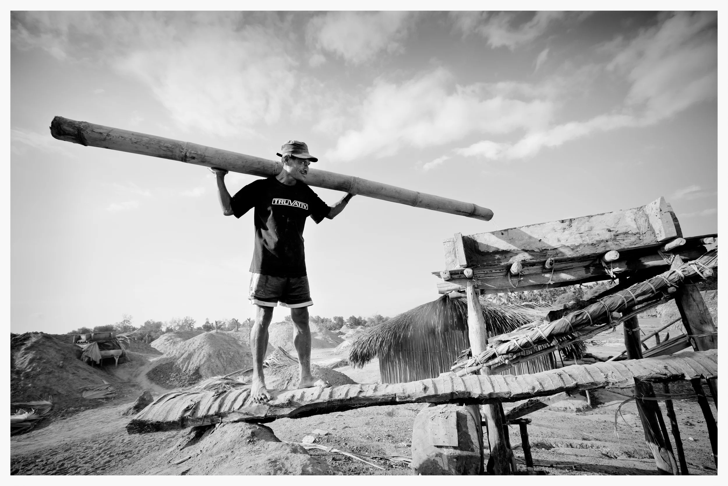 A salt-worker uses a bamboo tube to carry seawater to a clay filter. East Timor. Photo: © Marcus Perkins