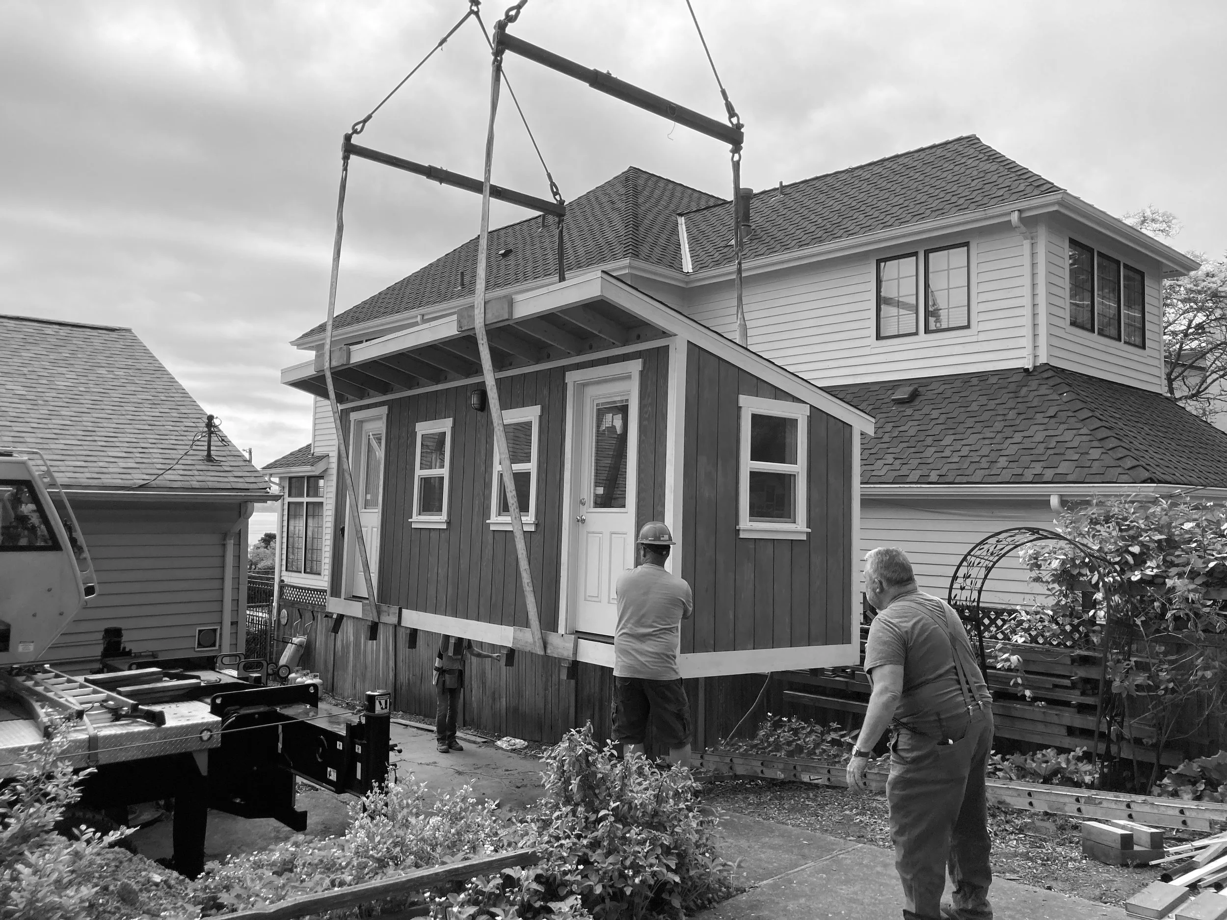 Construction workers installing a small wooden structure in the backyard of a house.