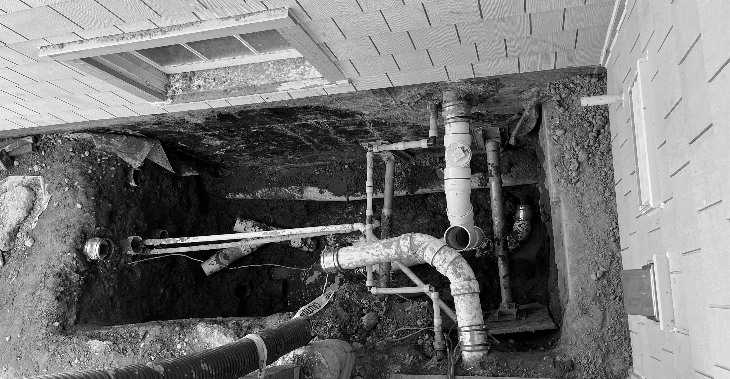 Underground plumbing pipes and valves in a trench at a construction site next to a building wall.
