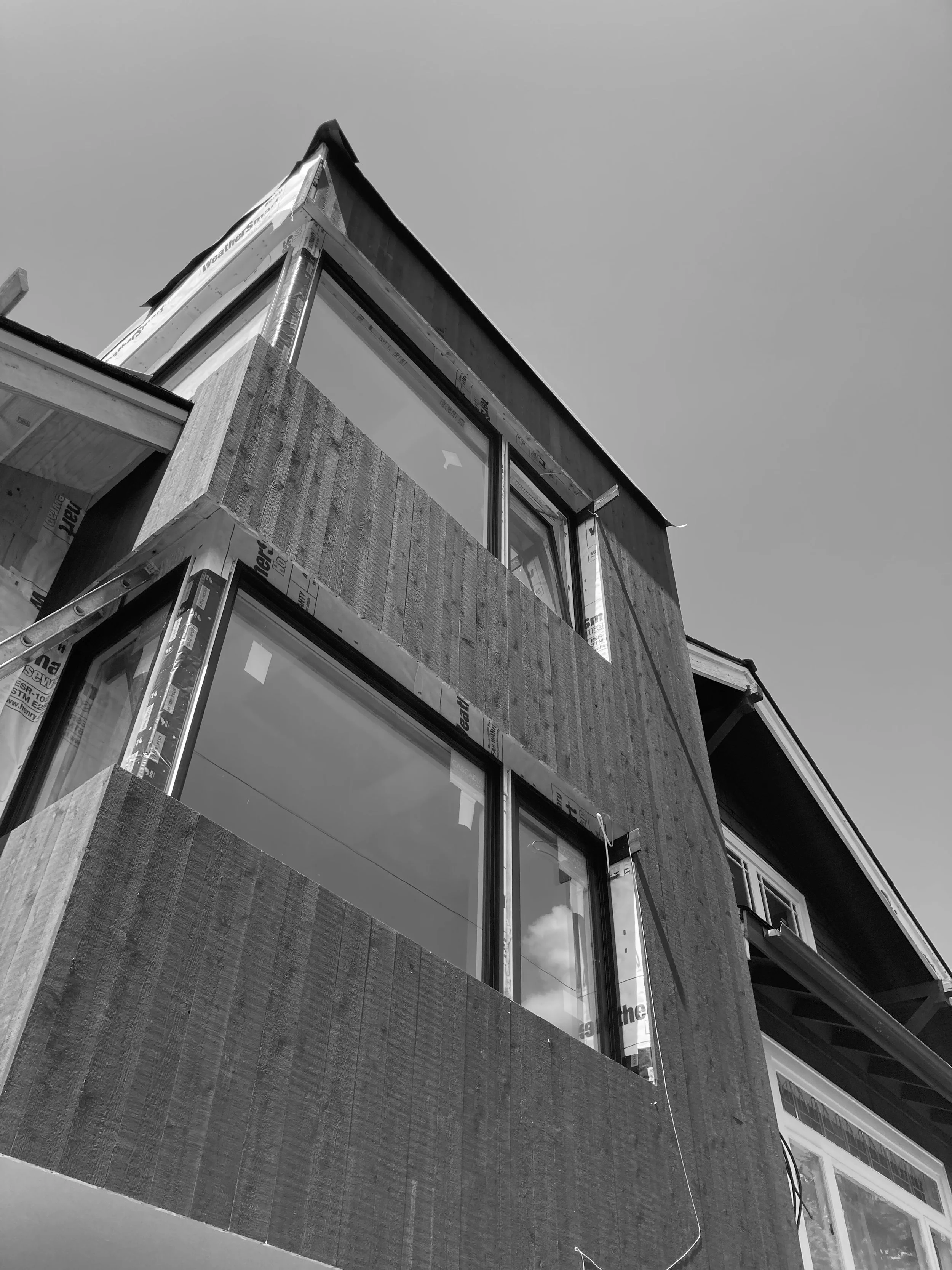 Black and white photo of a building under construction, showing large windows and unfinished exterior walls covered with weather-resistant material.