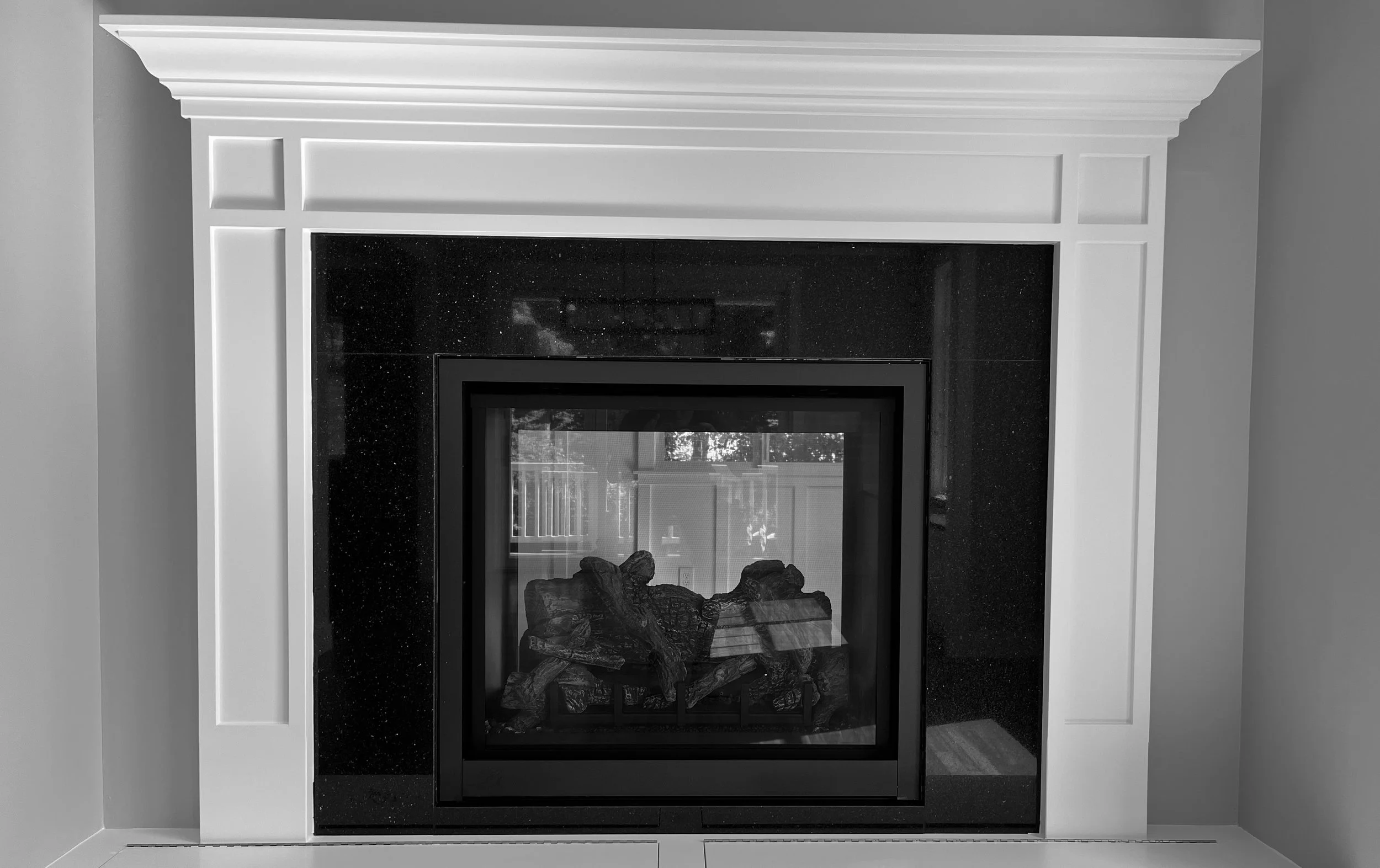 A modern fireplace with a white mantel, black marble surround, and glass-enclosed firebox with logs inside.