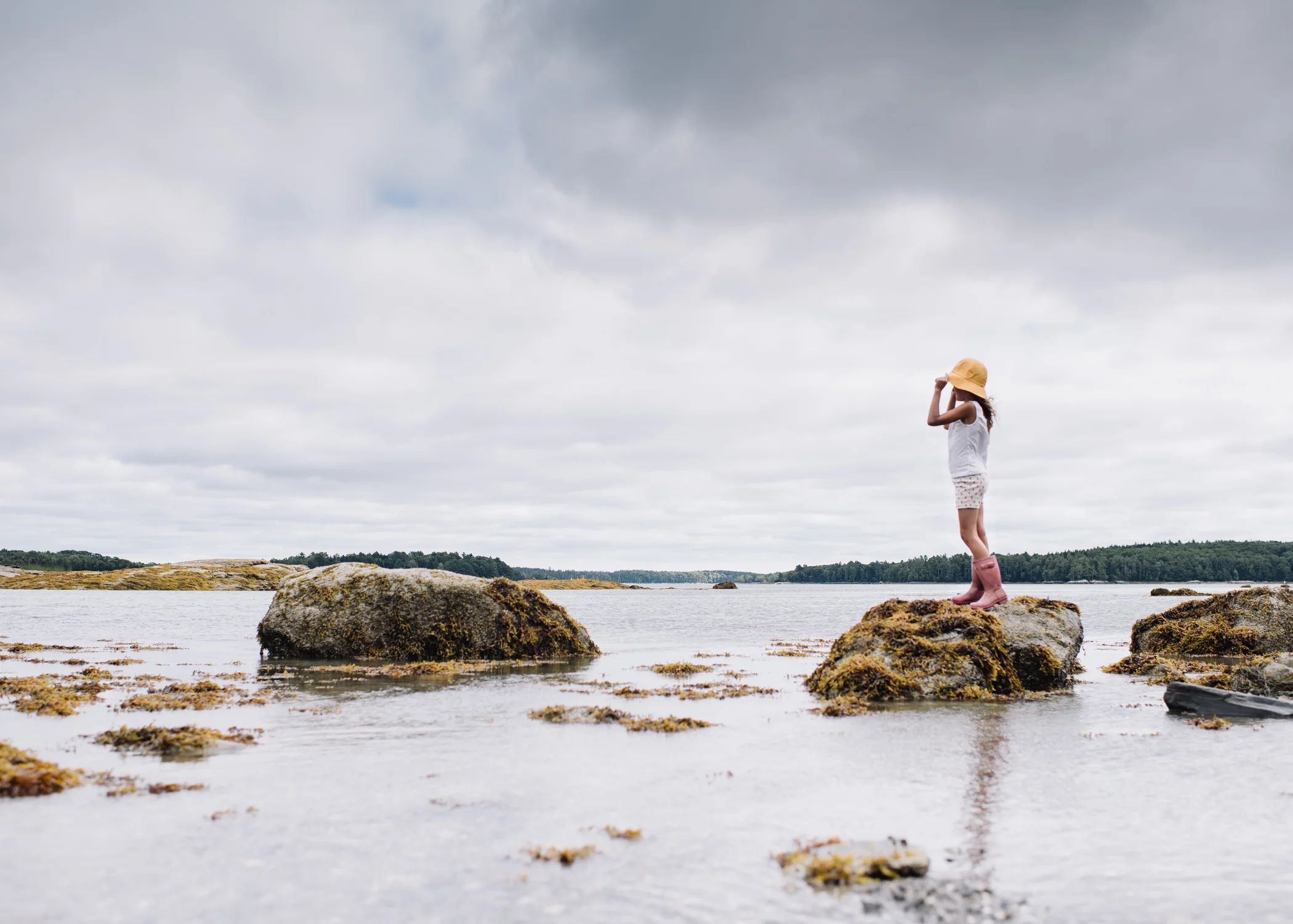 girl looking out to sea standing on the rocks on a stormy day - maine children's portrait photography