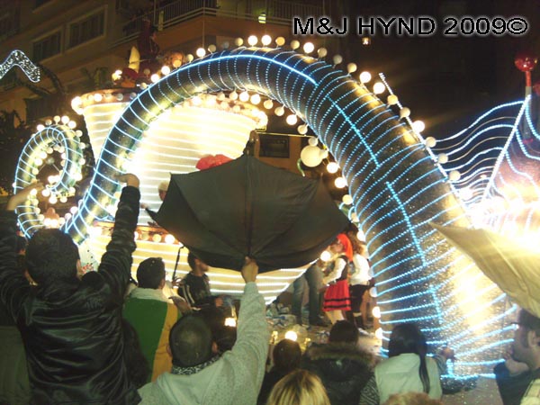 neon dragon tail / parade #8: Spain Alicante Los Reyes Magos Three Kings' Fiesta Spanish Epiphany Christmas season, holiday parade, spectators, float raining presents upturned umbrella