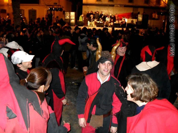 blk/red with horns: spain Alicante Carnival Fiesta, Costa Blanca, darkened plaza, bright-lit stage, spectators dressed in black and red, dance court jester with gold horns