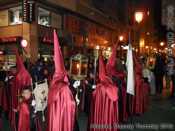  spain Alicante, Semana Santa Holy Week, Maundy Thursday procession, Brotherhood long pointed red hood, long capes carry lamps on poles, flag-bearers, somber march 