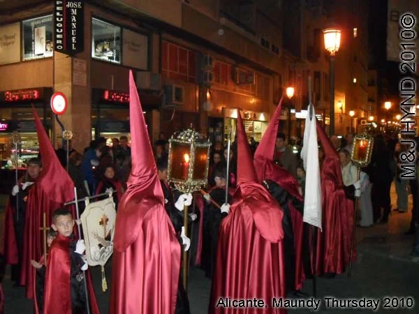 spain Alicante, Semana Santa Holy Week, Maundy Thursday procession, Brotherhood long pointed red hood, long capes carry lamps on poles, flag-bearers, somber march
