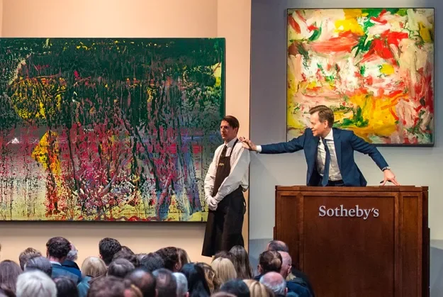 An auction at Sotheby's with two men presenting colorful abstract paintings to an audience.