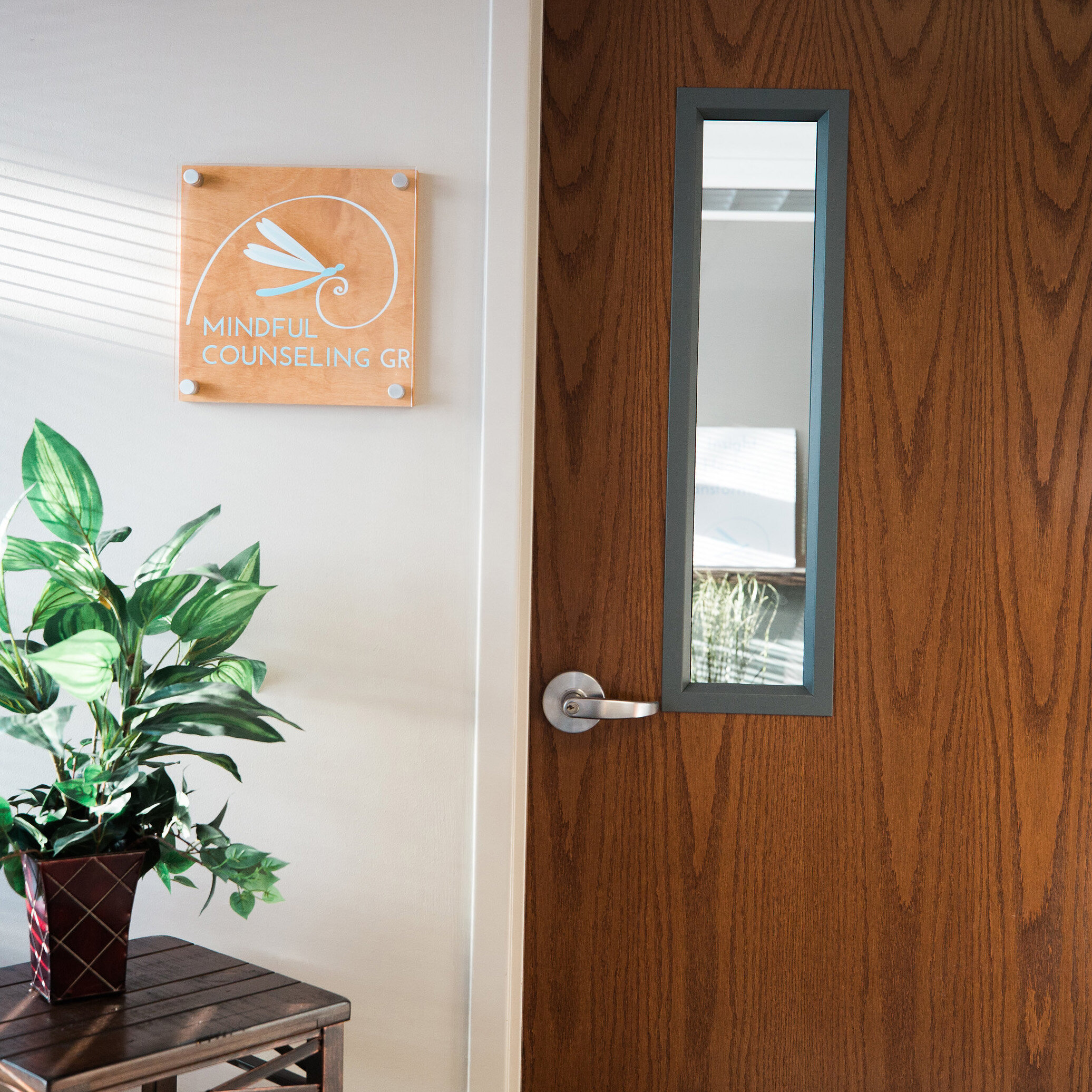 Exterior of a mindful counseling GR office with a logo sign on the wall and a plant under it on a side table.