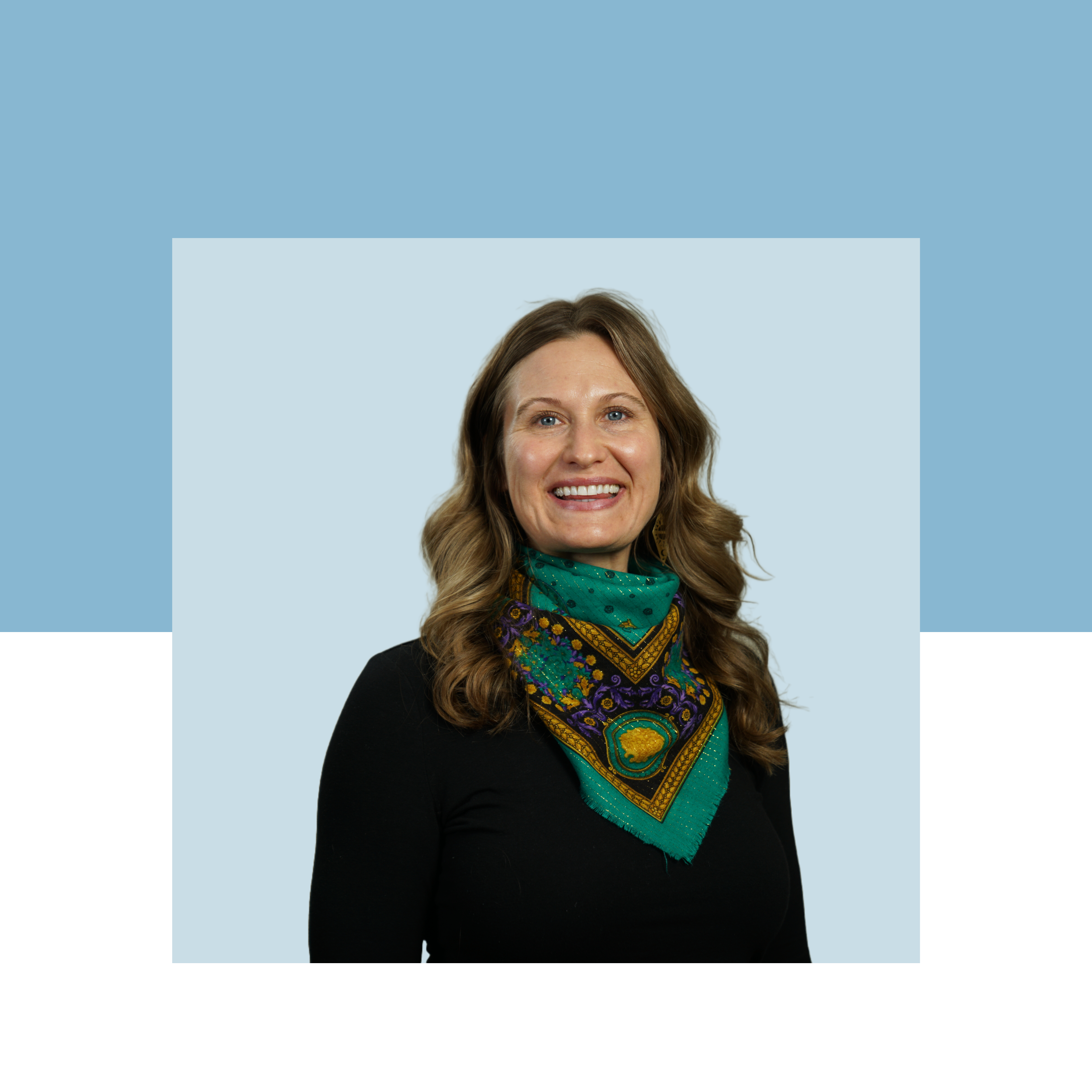 Woman smiling with shoulder length brown hair. She wears a black shirt and silk green scarf around her neck.