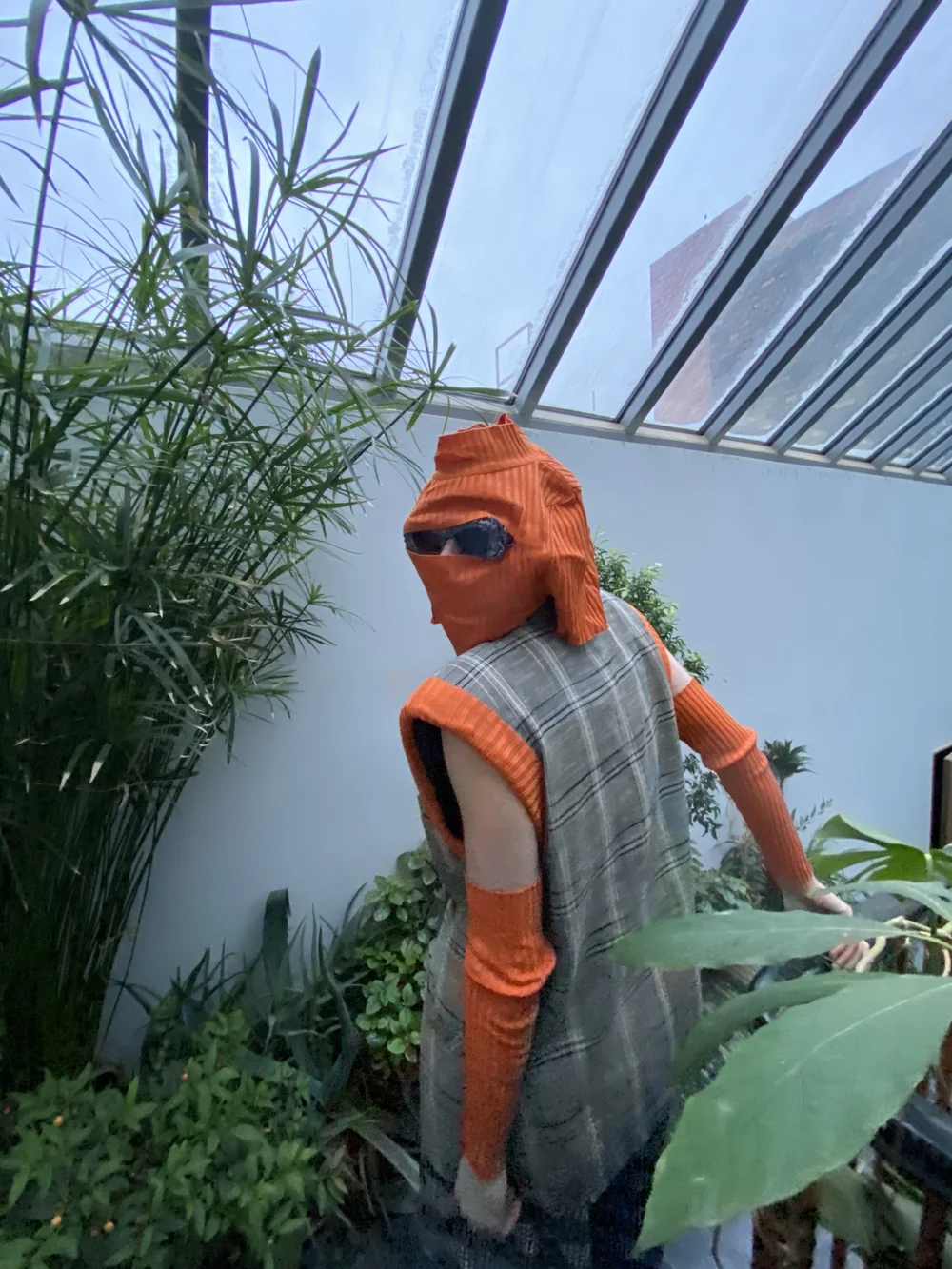  Garment description: Beige plaid double-breasted suit jacket vest with upcycled orange sweater as thick trim on armoles. Sweater sleeves worn as arm coverings, and sweater body worn as balaclava. Blue lace embellished sunglasses poke through eye sli