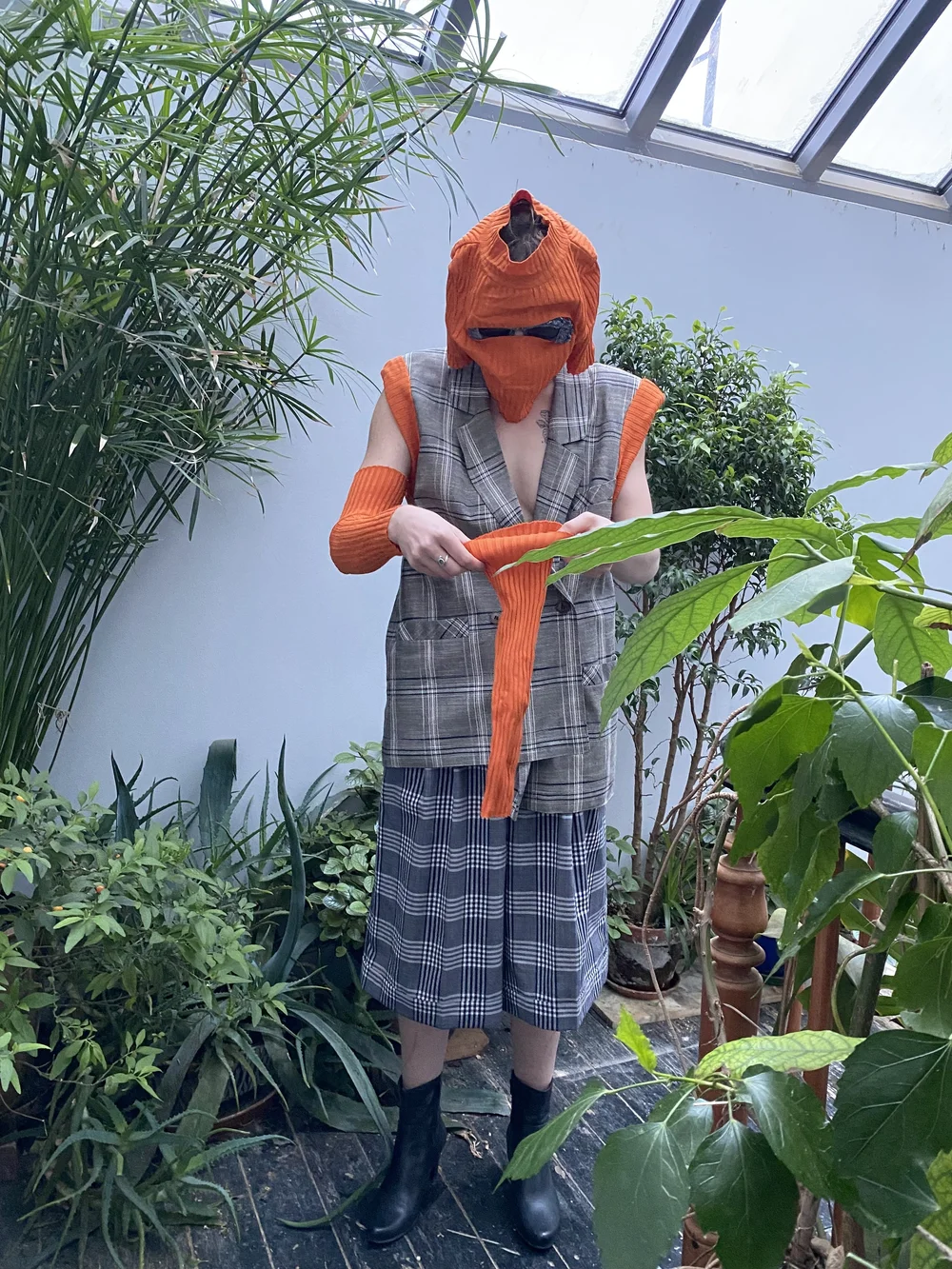  Garment description: Beige plaid double-breasted suit jacket vest with upcycled orange sweater as thick trim on armoles. Sweater sleeves worn as arm coverings, and sweater body worn as balaclava. Blue lace embellished sunglasses poke through eye sli