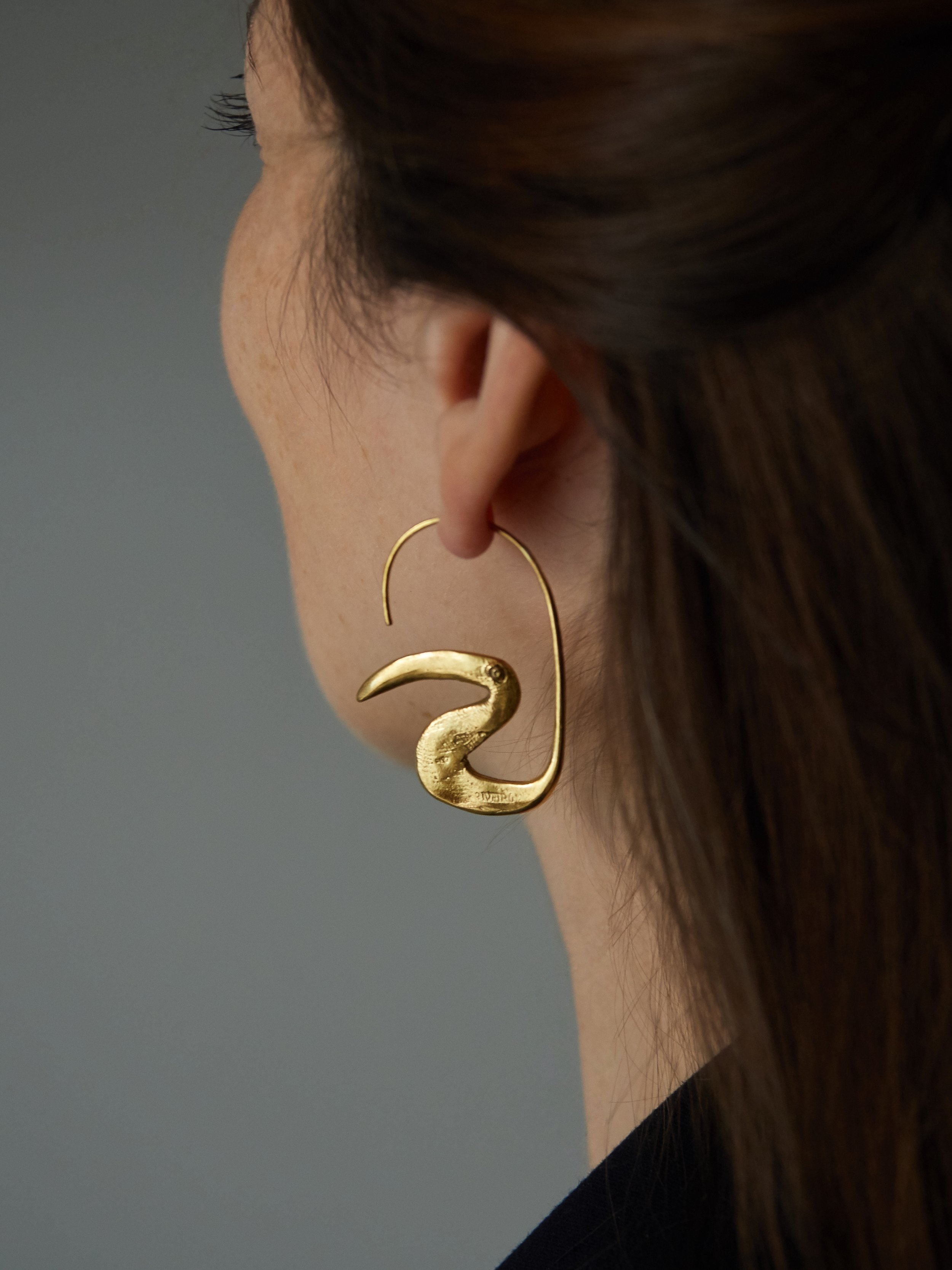 Gold-plated bronze Toucan earrings by French jewellery designer Elisabeth Riveiro, featuring a sculptural bird silhouette with a curved beak and elongated ear wire.