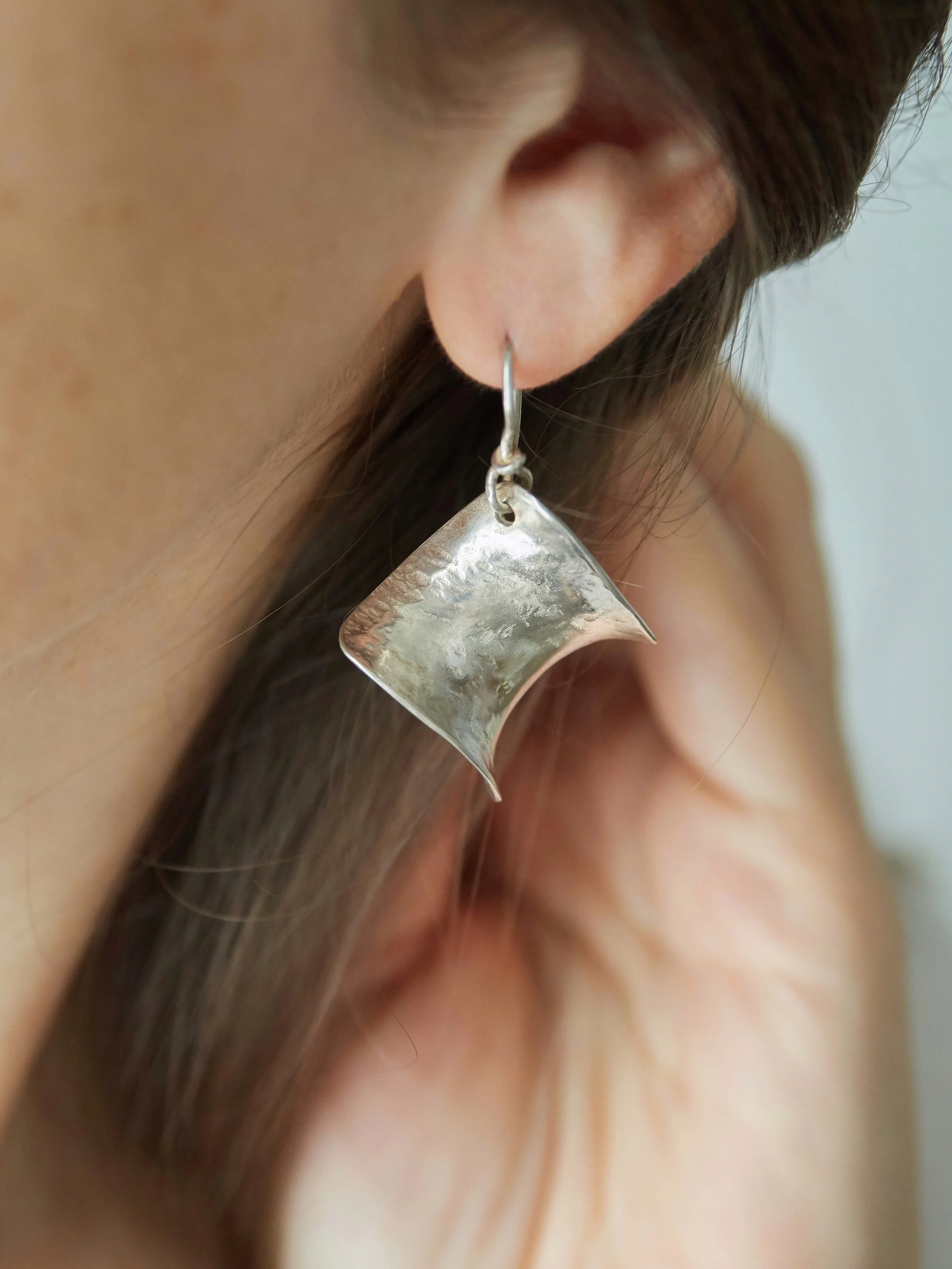 Close-up of Petite Éole silver-plated bronze earrings by Elisabeth Riveiro, showing their hammered surface and softly curved geometric silhouette.