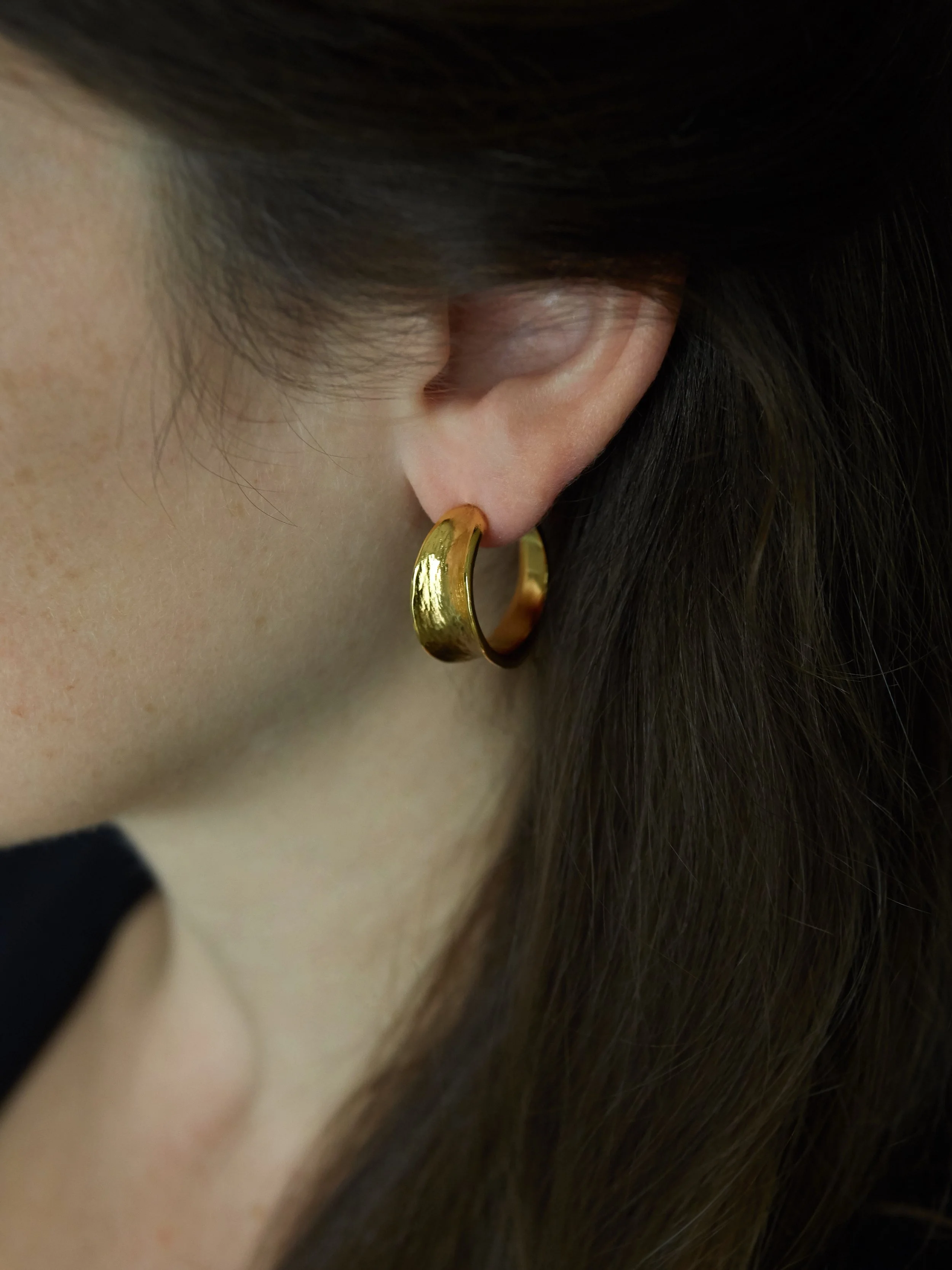 Gold-plated bronze Petit Val sculptural hoop earring by Elisabeth Riveiro, worn on the ear. Handcrafted in Paris using traditional lost-wax casting, featuring an organic shape and hammered finish.