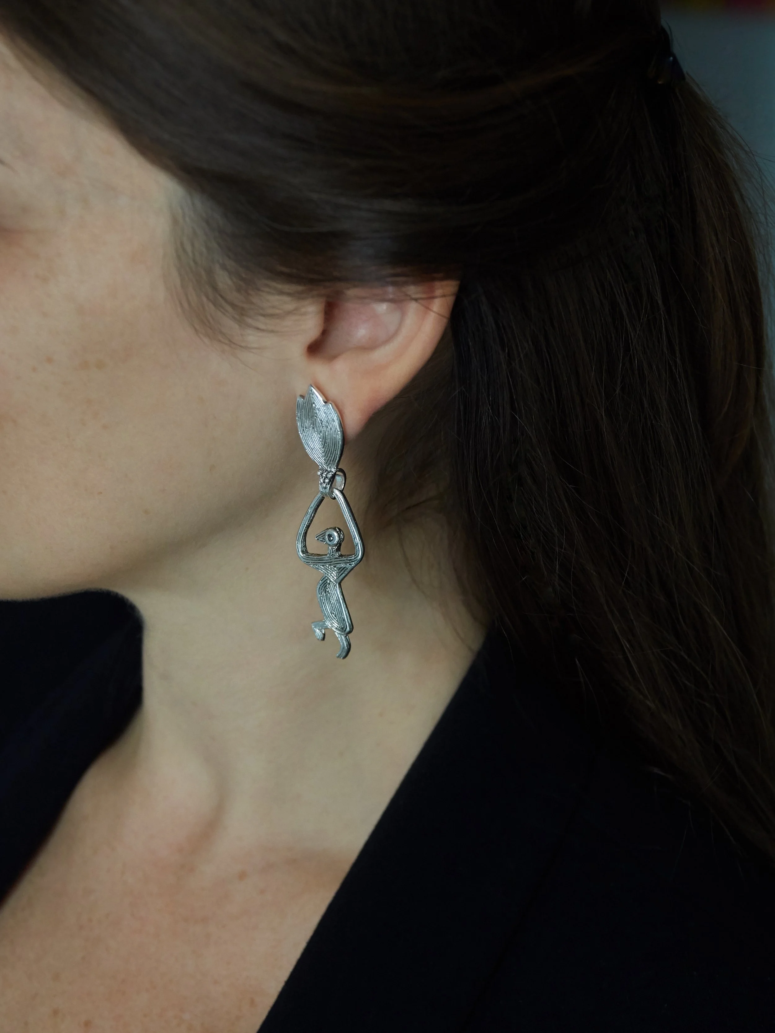 Elisabeth Riveiro’s Isadora Double dangling earrings in silver-plated bronze, featuring a stylised human figure suspended from a textured leaf-shaped element, shown worn on the ear.