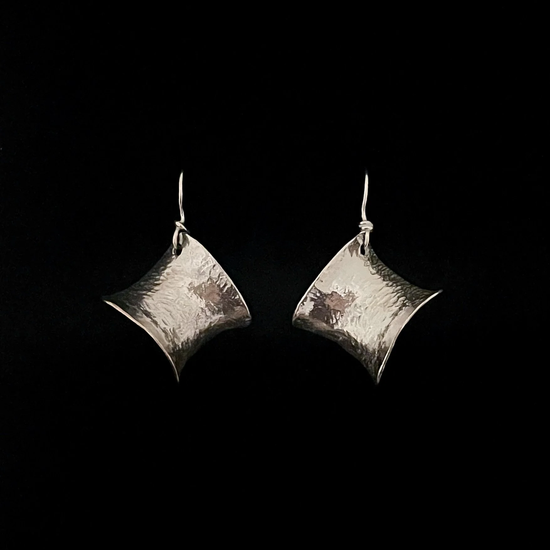 Pair of Petite Éole earrings by Elisabeth Riveiro in silver-plated bronze, featuring curved geometric pendants with hammered surfaces and French hook ear wires.