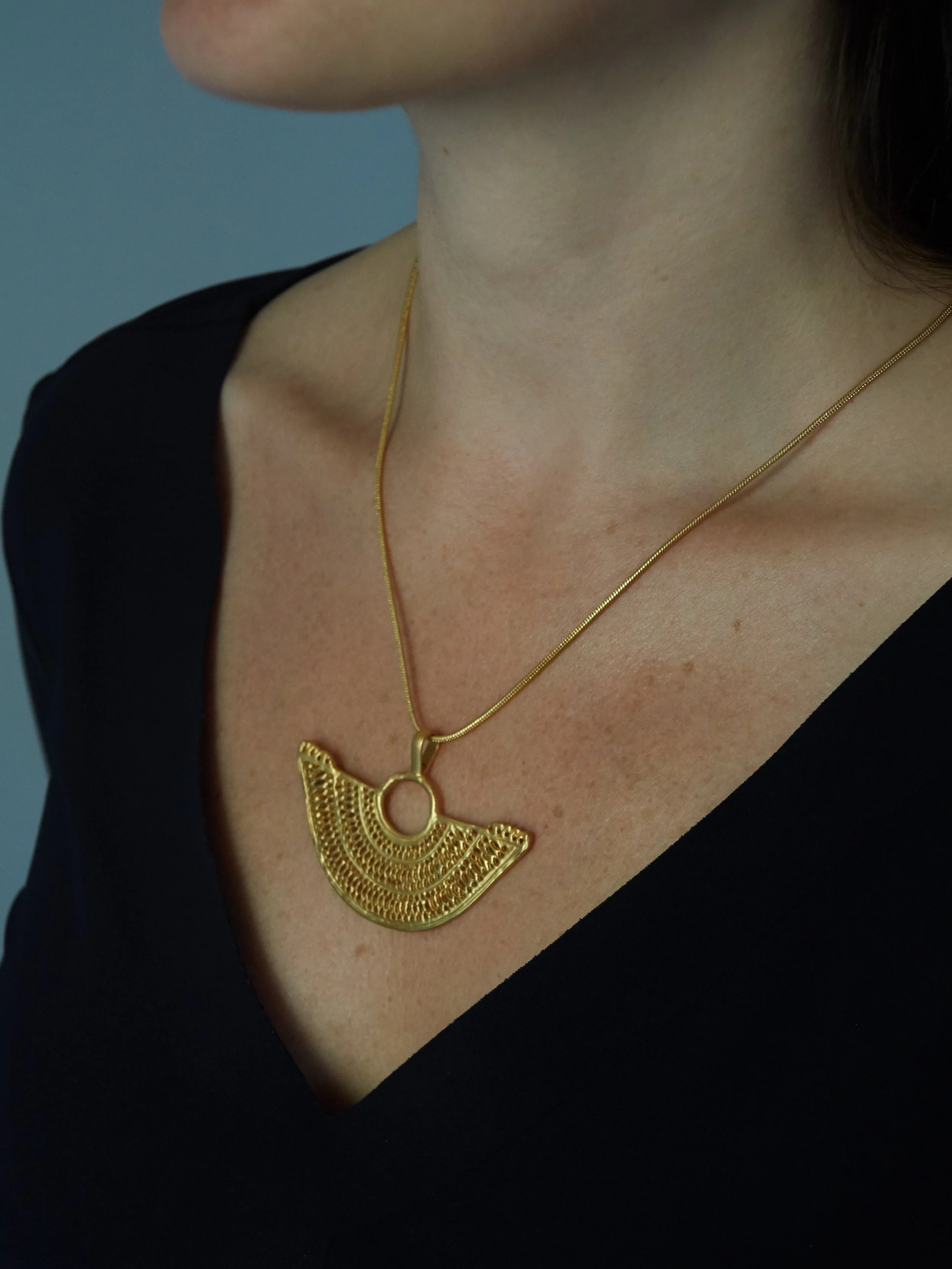 Zenú-inspired gold-plated cast filigree pendant with intricate openwork pattern, worn on a gold-toned chain.