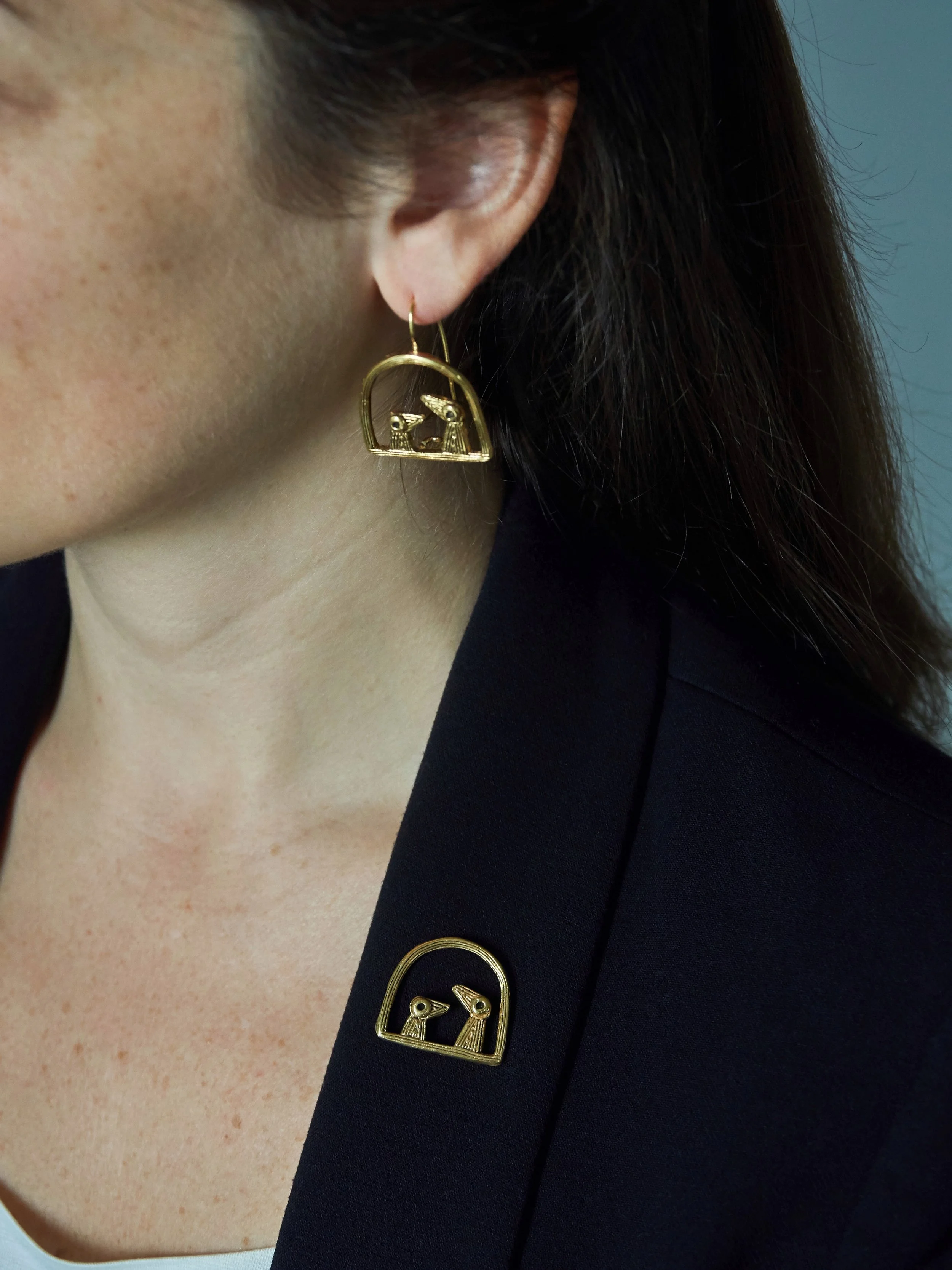 Elisabeth Riveiro “Père et Fils” bird fibula brooch in gold-plated bronze, handcrafted using the lost-wax technique, worn on a dark blazer at AMBART Palma de Mallorca.