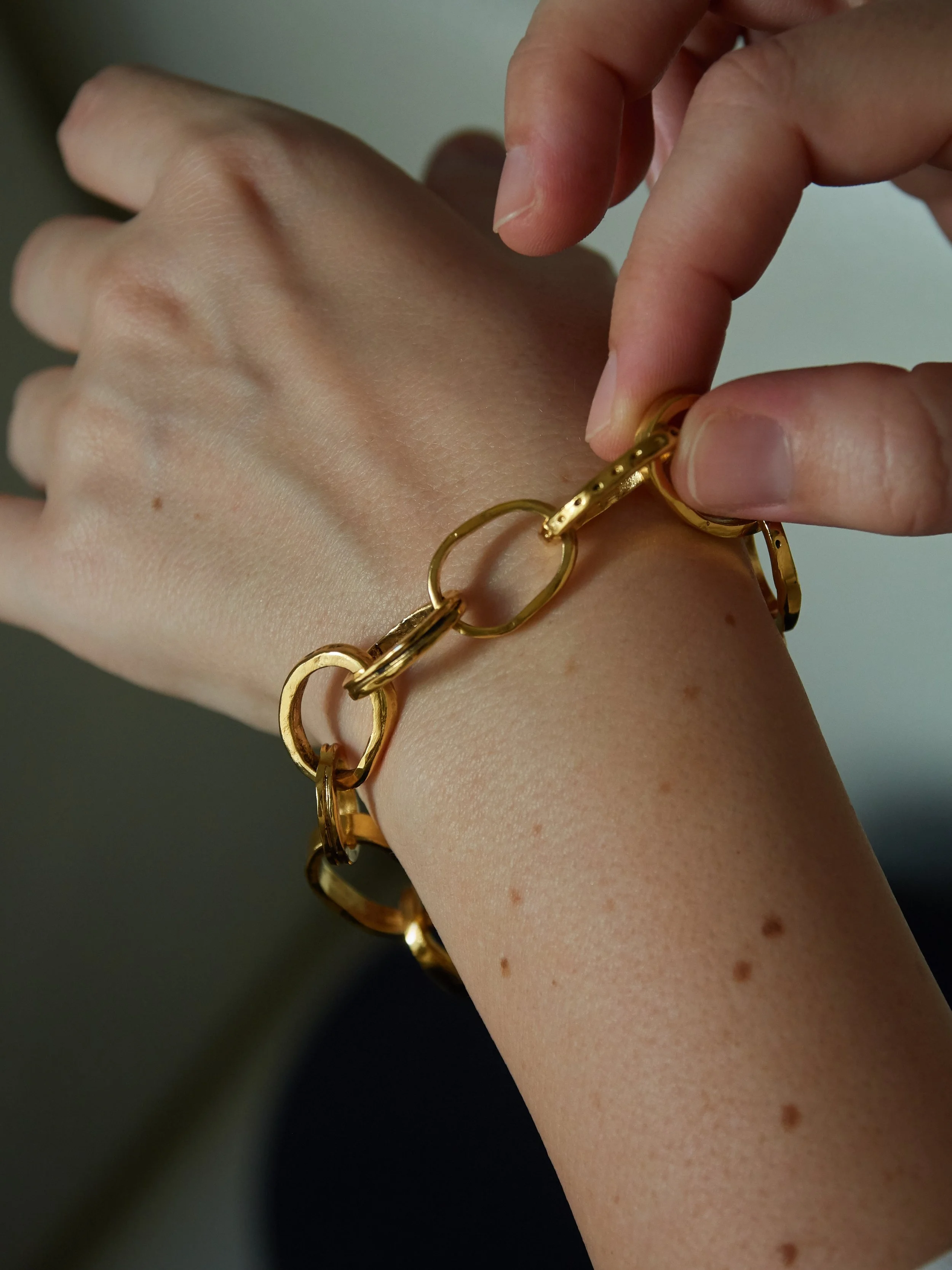 Close-up of the CHAINETTE gold-plated bronze bracelet by Elisabeth Riveiro, highlighting its irregular interlocking oval links and handcrafted finish.