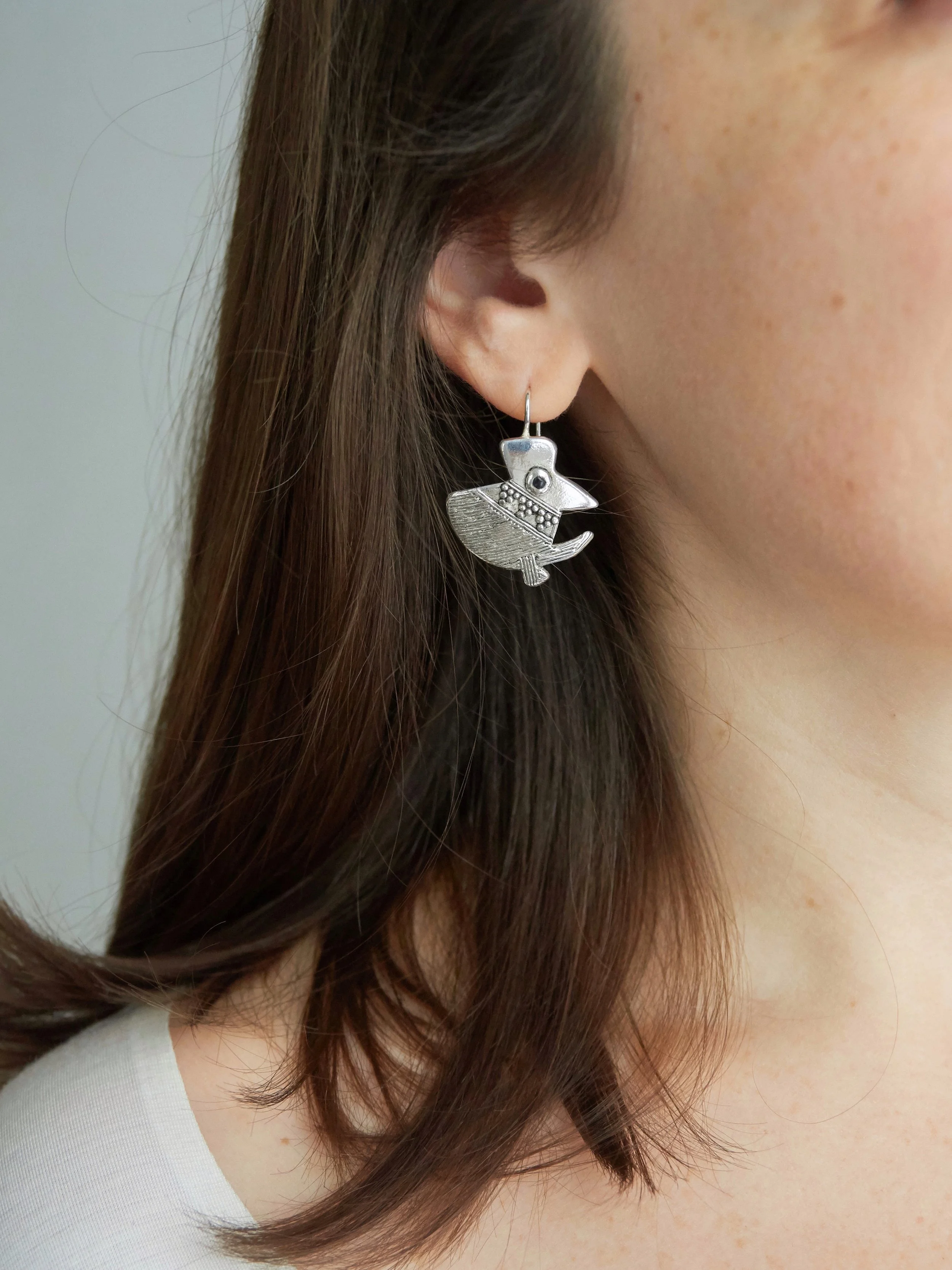 Silver-plated bronze Piano bird earring by Elisabeth Riveiro, featuring a whimsical bird silhouette with textured wings and a dark enamel eye, shown worn by a model.