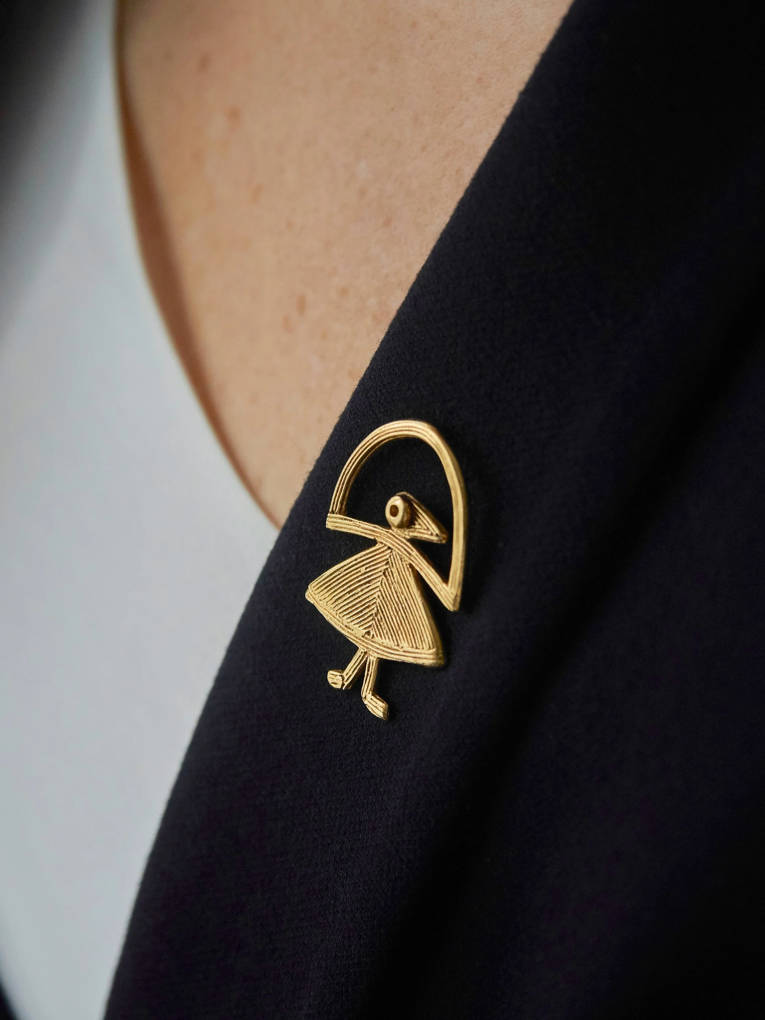 Elisabeth Riveiro “Elastis” fibula brooch pin in gold-plated bronze, handcrafted using the lost-wax technique, worn on a dark blazer at AMBART Palma de Mallorca.