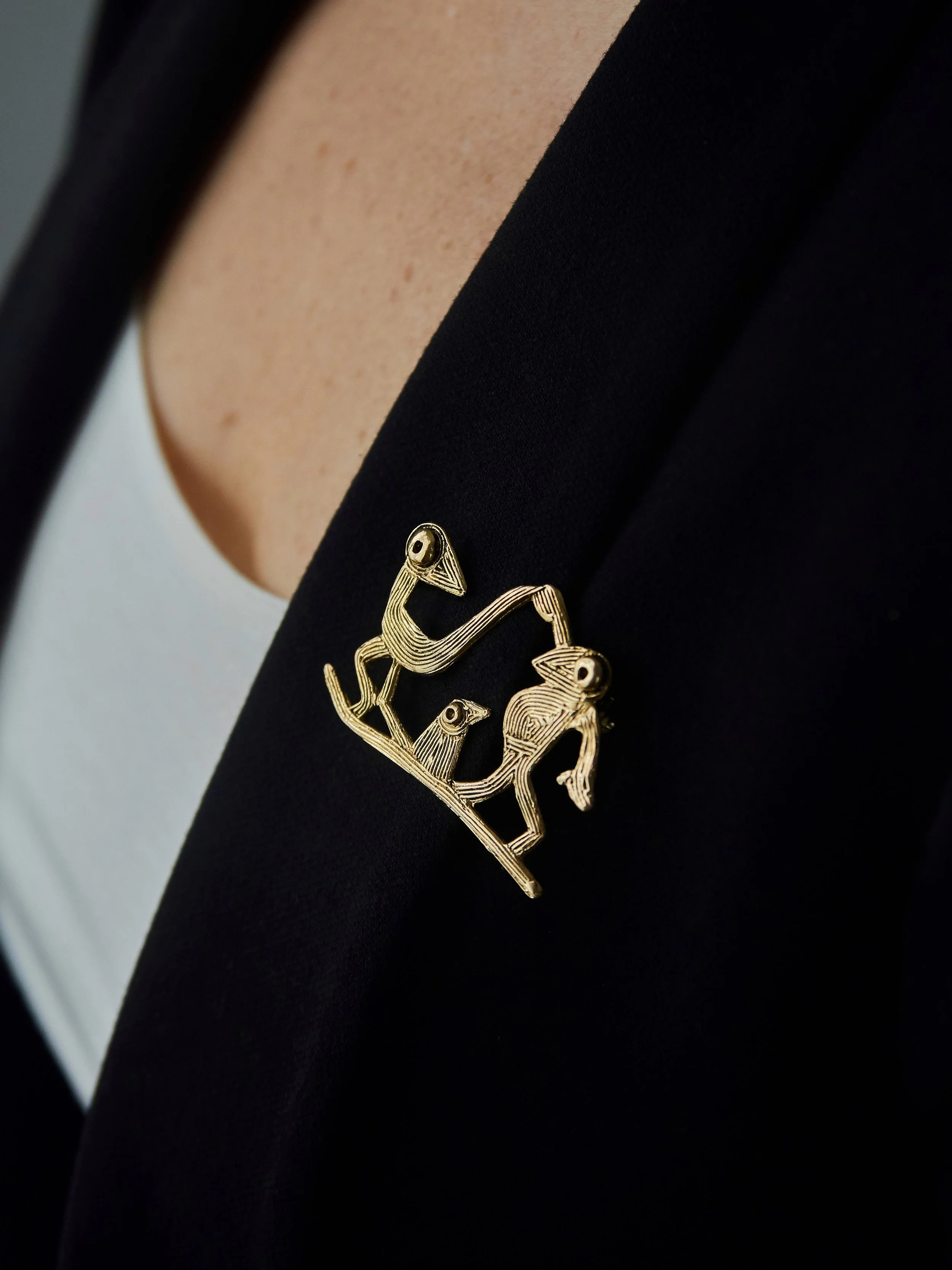 Farandole bronze bird brooch by Elisabeth Riveiro, handcrafted using the lost-wax technique, worn on a black blazer lapel.