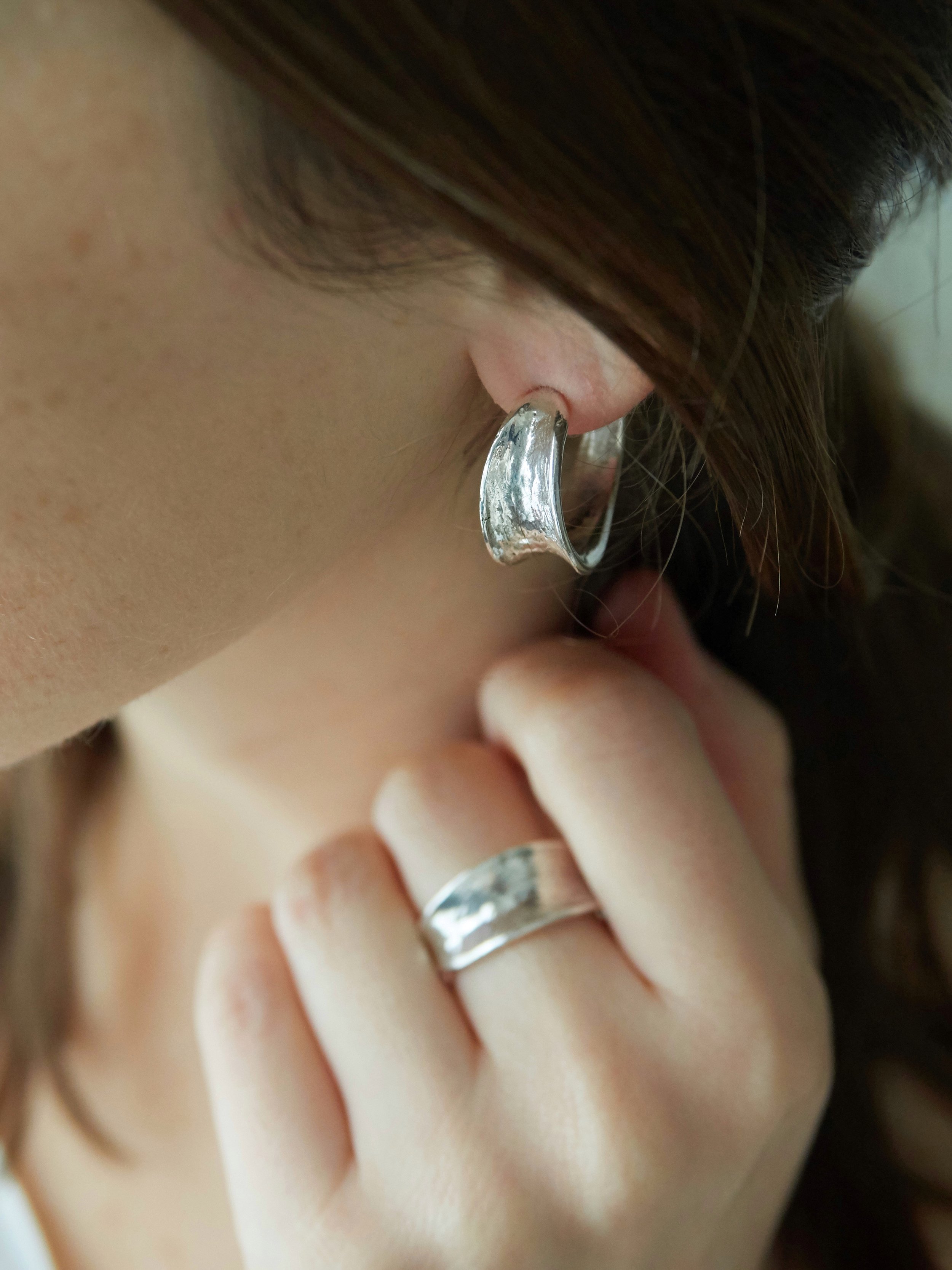 Petit Val silver-plated bronze sculptural hoop earring worn with a matching hammered ring by Elisabeth Riveiro. Contemporary handcrafted jewellery with organic textures.