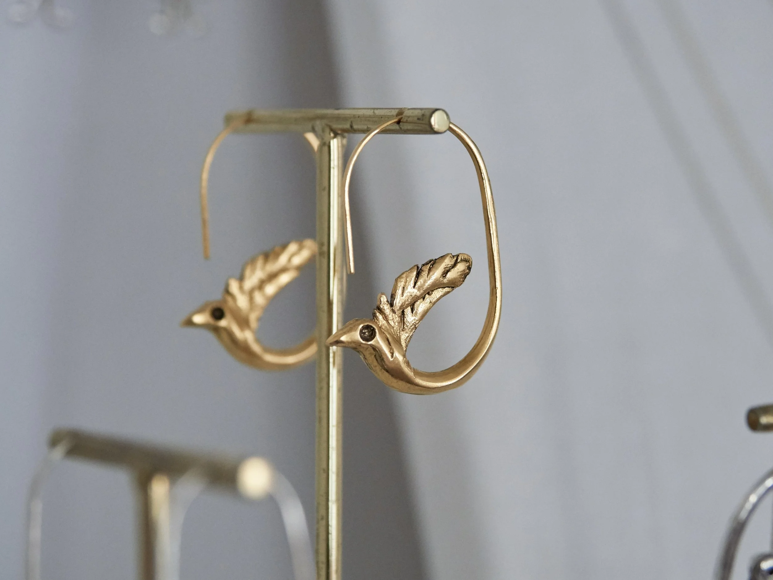 Gold-plated bronze bird earrings by Elisabeth Riveiro on display stand, handcrafted lost-wax casting jewellery