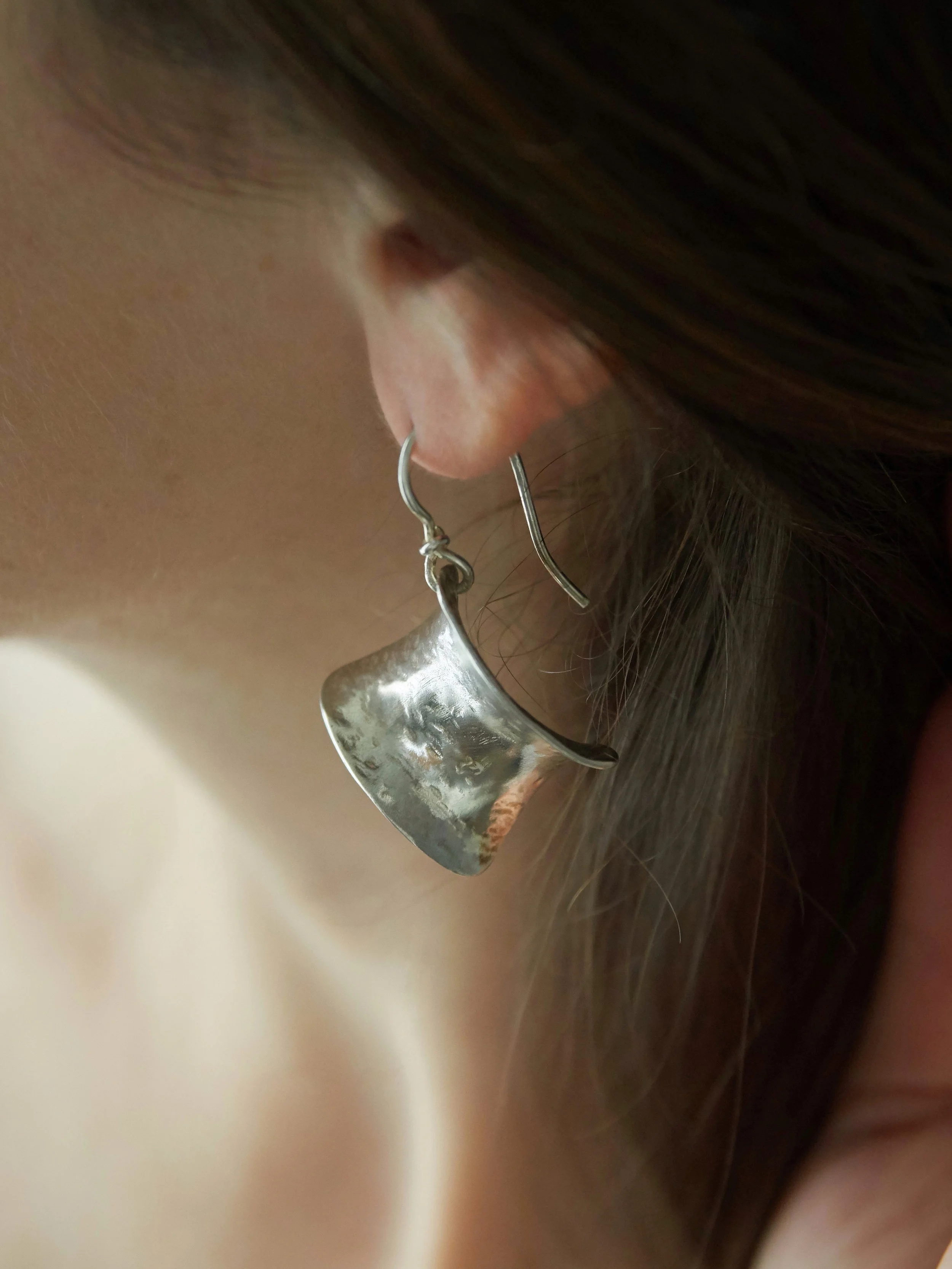 Side view of Elisabeth Riveiro Petite Éole earrings in silver-plated bronze, highlighting their curved sculptural form and suspended French hook design.