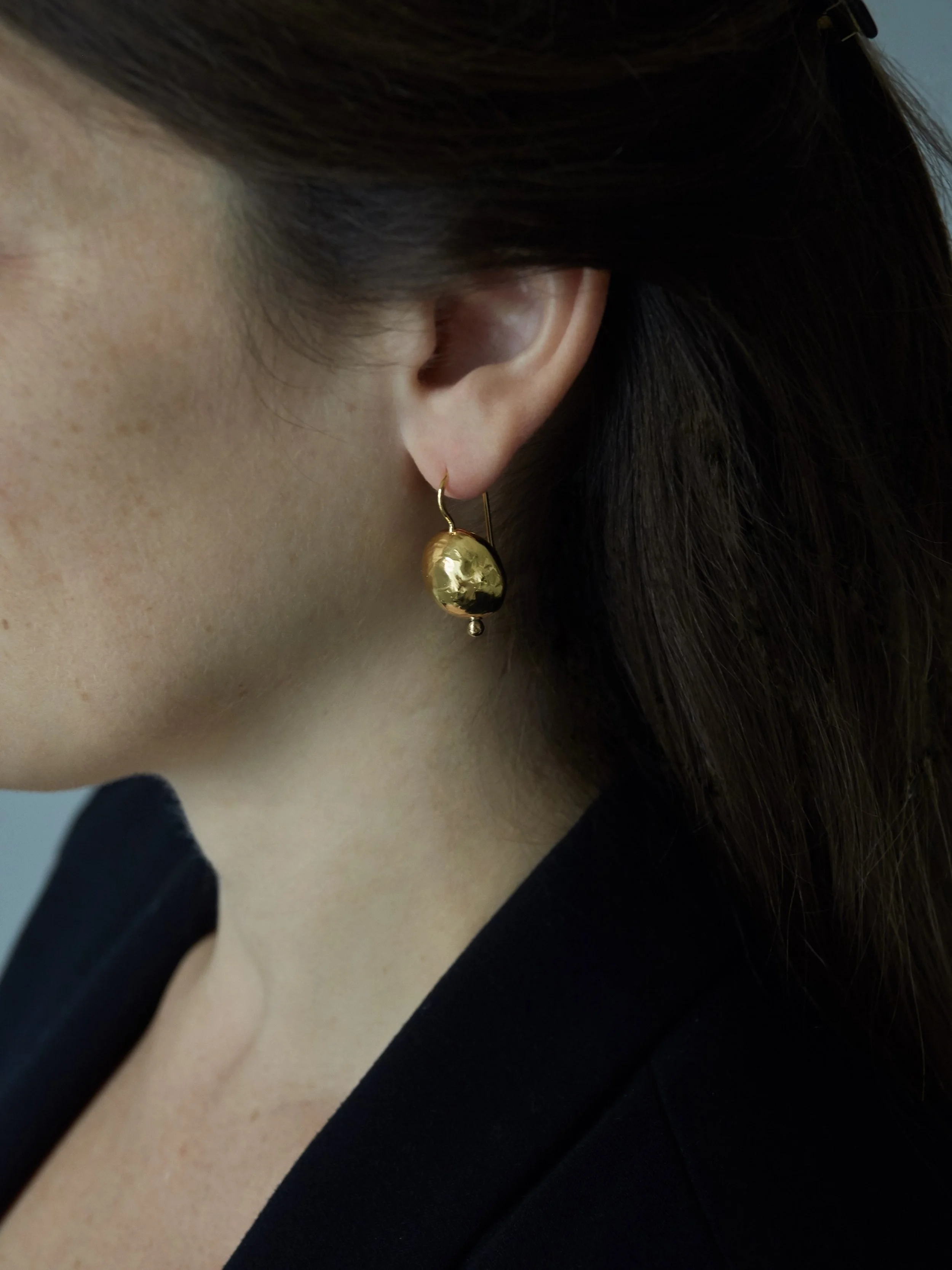 GRANDES SPHÈRES hammered gold-plated bronze earring by Elisabeth Riveiro, shown worn from the side.