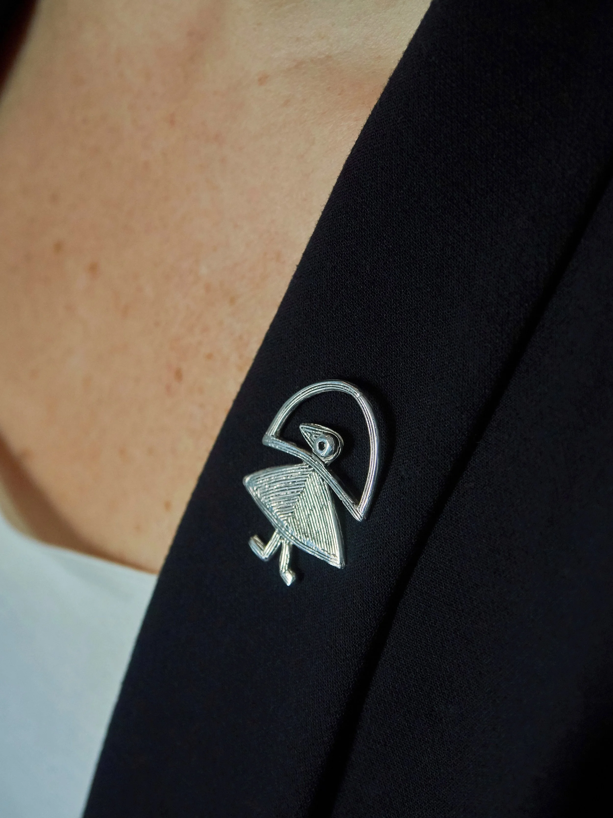 Elisabeth Riveiro “Elastis” fibula brooch pin in silver-plated bronze, handcrafted using the lost-wax technique, worn on a dark blazer at AMBART Palma de Mallorca.